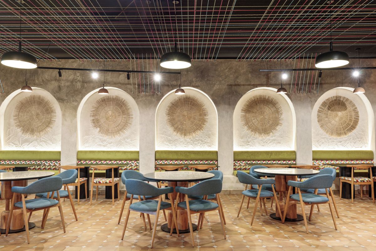 Interior de restaurante com mesas redondas e cadeiras azuis, piso com padrão decorativo e luminárias no teto.