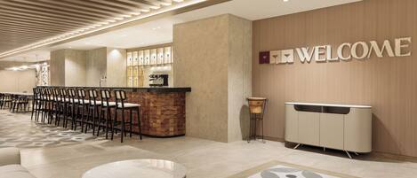 A modern hotel lobby with a reception desk, a bar area, and a seating area with a patterned rug.