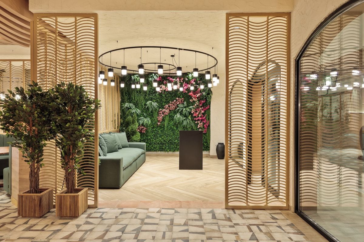A modern interior with a green sofa, wooden partitions, a circular light fixture, and a green wall with plants.