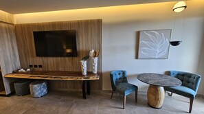 Une chambre moderne avec un mur d’accent en bois, un téléviseur à écran plat, une table à manger avec des chaises et une table basse ronde.