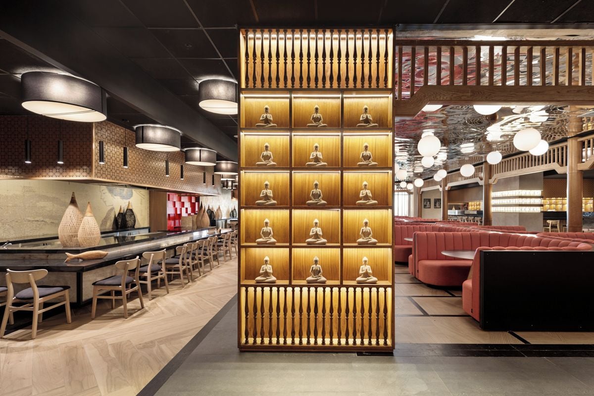 A modern interior with a central wall of illuminated statues, seating areas, and a bar.