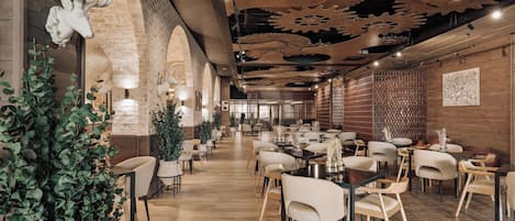 A restaurant interior with wooden walls, a brick fireplace, and a ceiling with large gears. Tables and chairs are arranged for dining.
