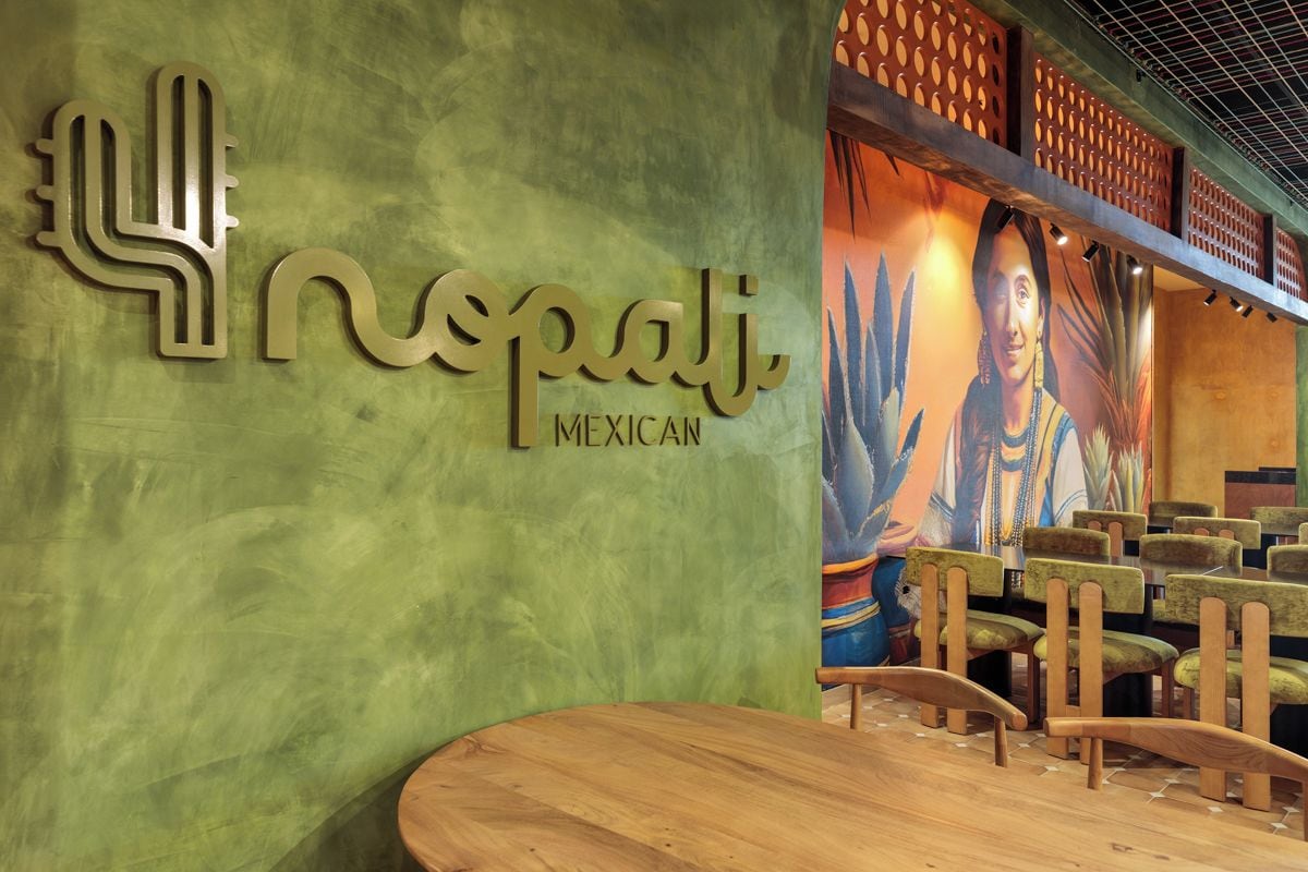 L’intérieur d’un restaurant avec un mur vert, une grande fresque murale et des meubles en bois.