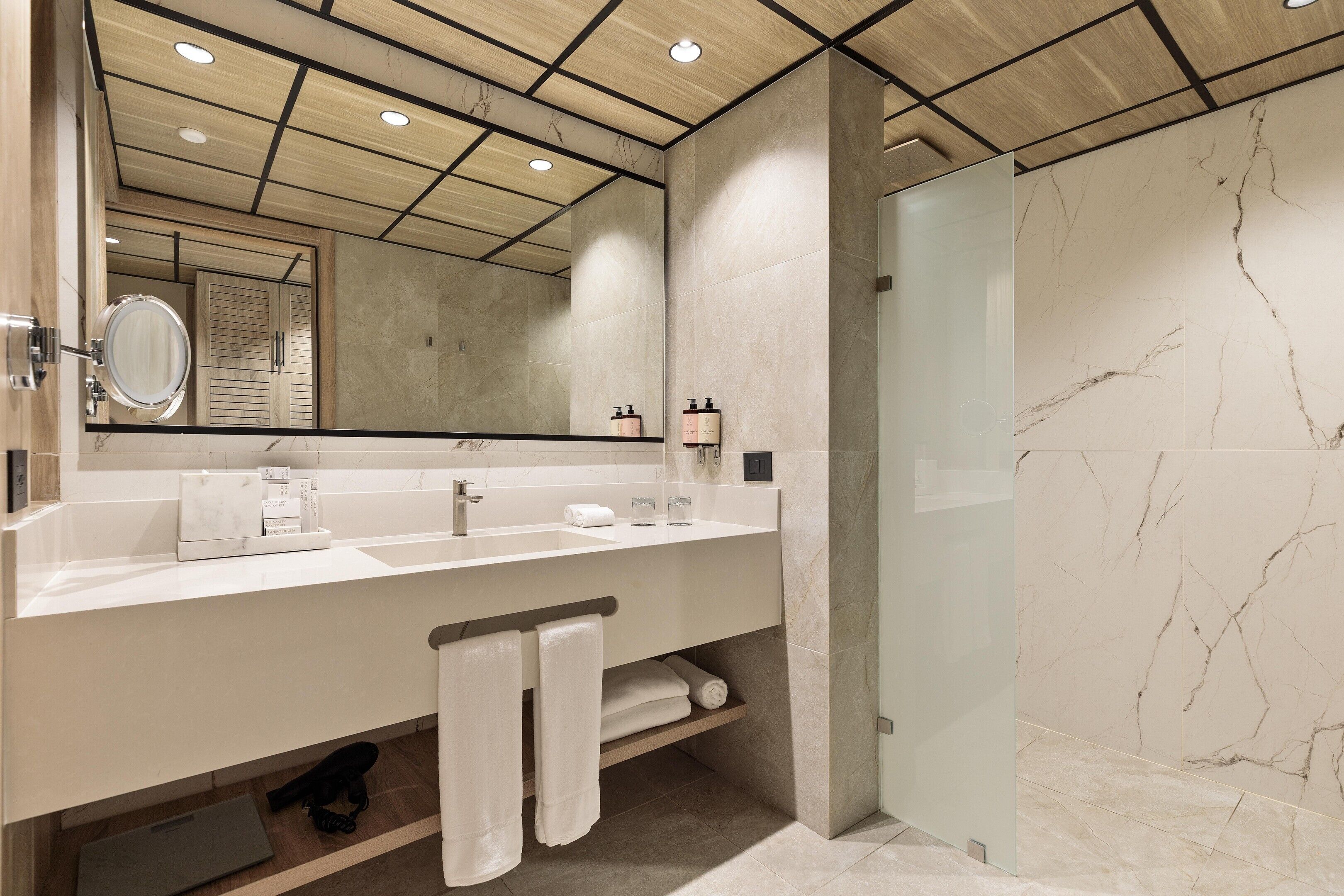 Une salle de bain moderne avec un grand miroir, deux vasques, une douche en verre et des murs en marbre.