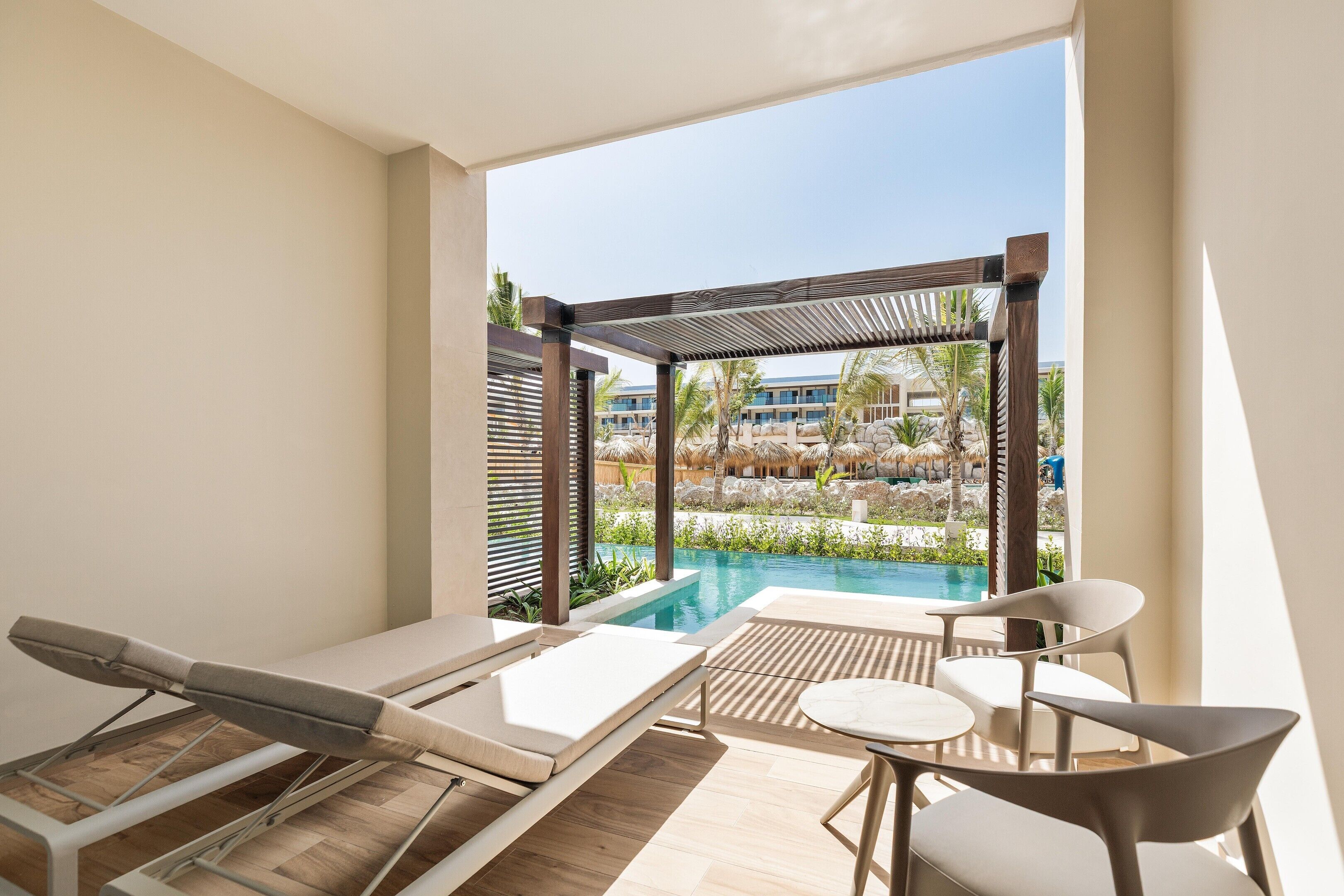 A poolside area with lounge chairs, a table, and a view of a resort pool and buildings.