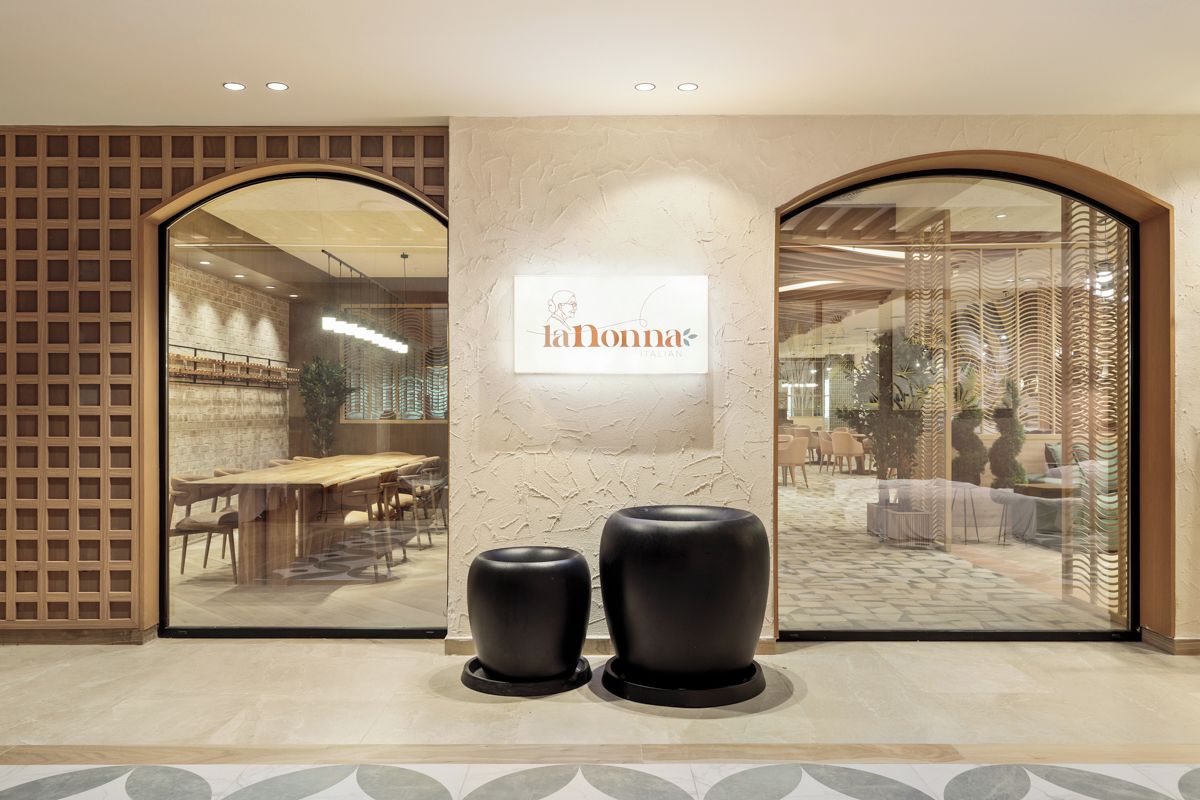 A restaurant entrance with a modern design, featuring a large glass window, a signboard, and two black stools in front.
