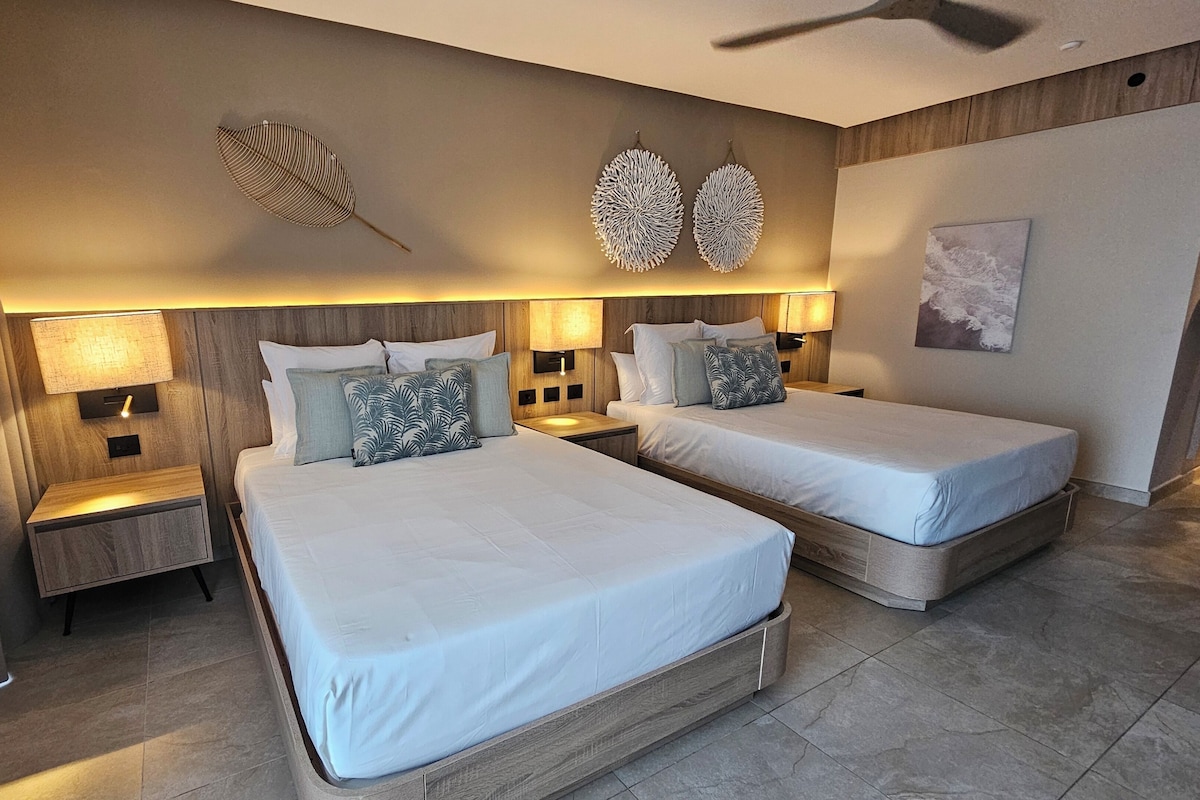 A hotel room with two beds, nightstands, wall-mounted lamps, and decorative wall art.