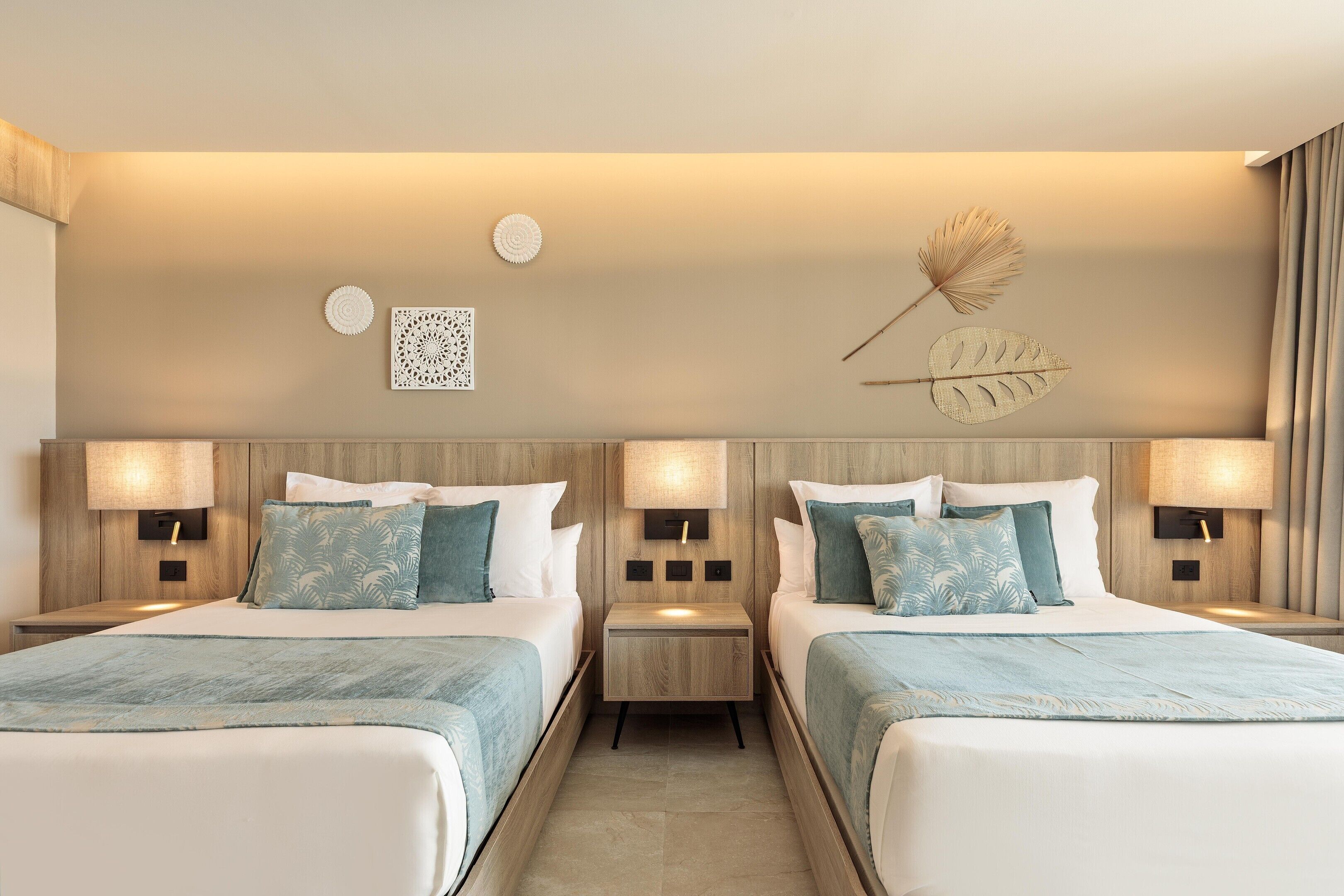 Una camera d'albergo con due letti, comodini, decorazioni a parete e un'ampia finestra con tende.