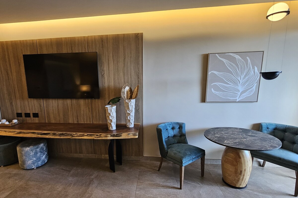 Una habitación moderna con pared de acento de madera, un televisor de pantalla plana, una mesa de comedor con sillas y una mesa redonda de centro.