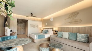 A modern hotel room with a bed, sofa, two tables, and decorative wall art. - Serenade Caribe Club Family Beach Resort – All Inclusive (Punta Cana)