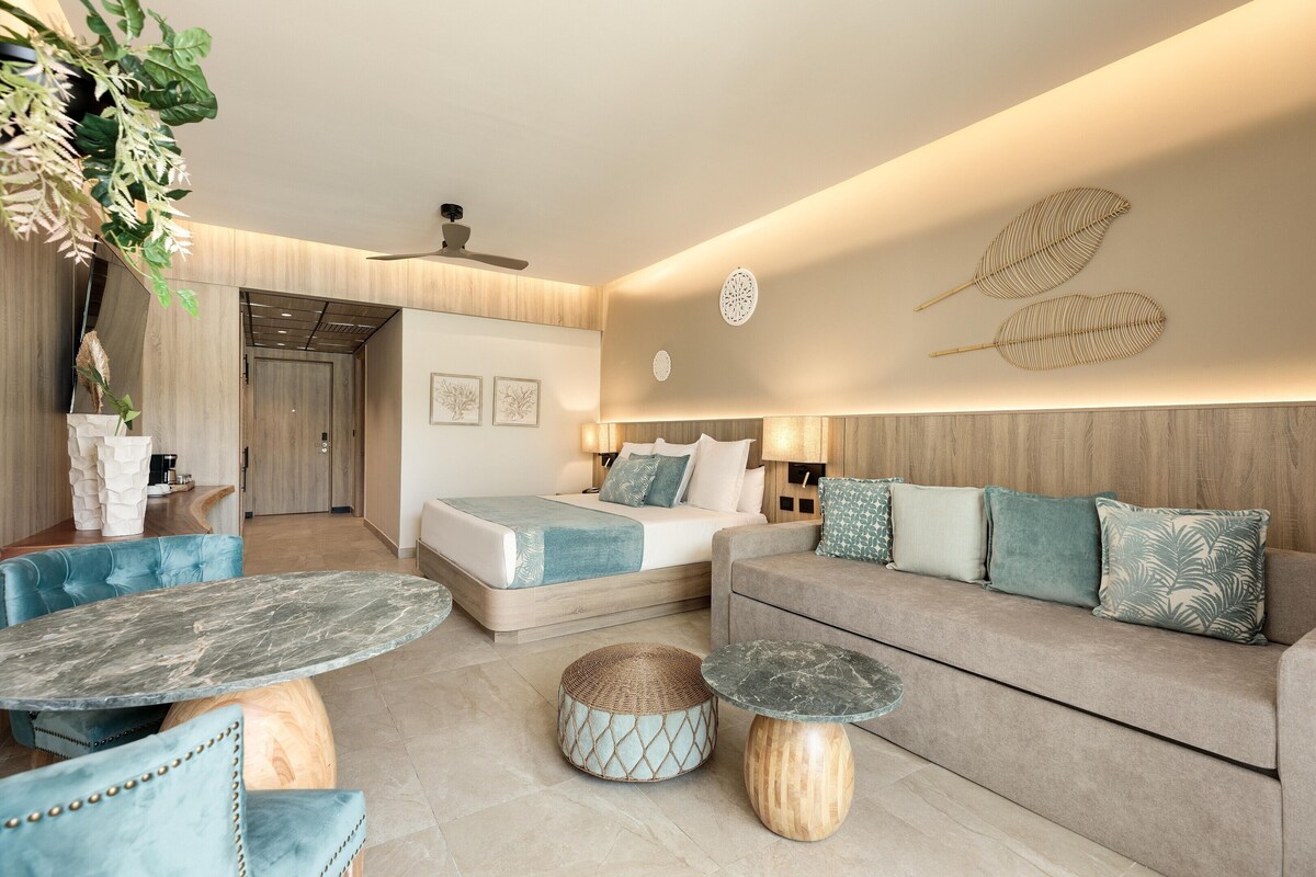 A modern hotel room with a bed, sofa, two tables, and decorative wall art.