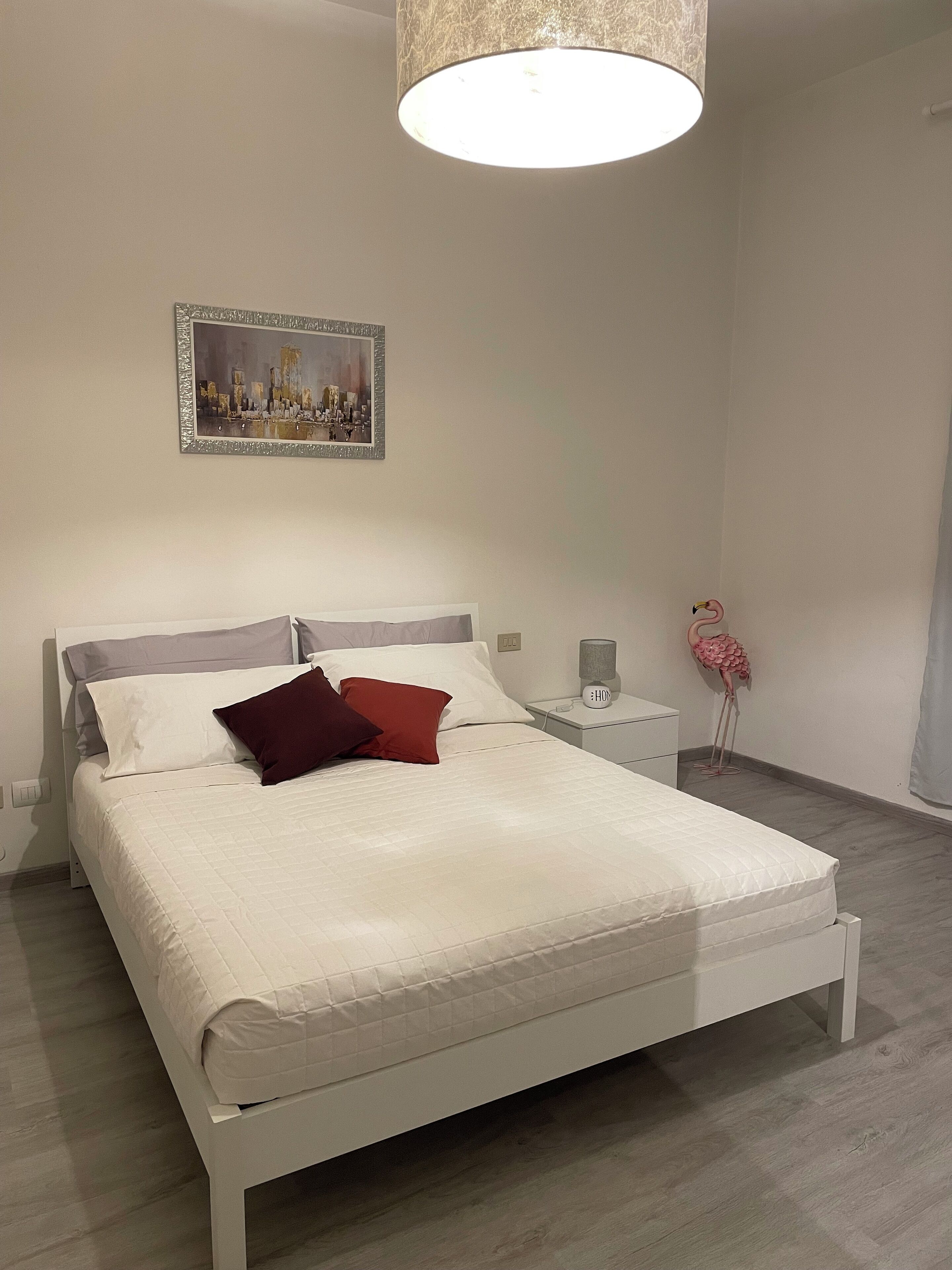 Una camera da letto ordinata con un letto, un comodino, una lampada e un quadro appeso al muro.
