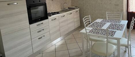 A modern kitchen with light wood cabinets, a built-in oven, a sink, and a dining table with chairs.