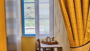 A room with a wooden floor, a table with chairs, a window with blinds, and a yellow curtain.