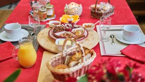 A breakfast table set with various food items, including pastries, fruits, and beverages, on a red tablecloth.