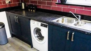Een kleine keuken met donkere kastjes, een roestvrijstalen spoelbak en een ingebouwde wasmachine.