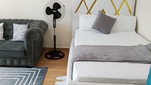 Quarto com cama, sofá cinza, ventilador e tapete estampado.