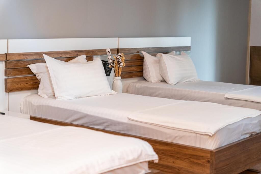 Habitación de hotel con dos camas, cabeceros de madera y un florero con flores secas en la mesita de noche.