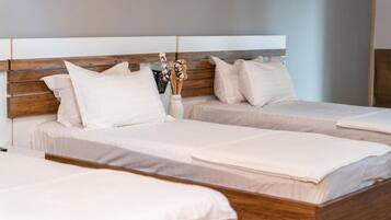 A hotel room with two beds, wooden headboards, and a vase with dried flowers on the nightstand.