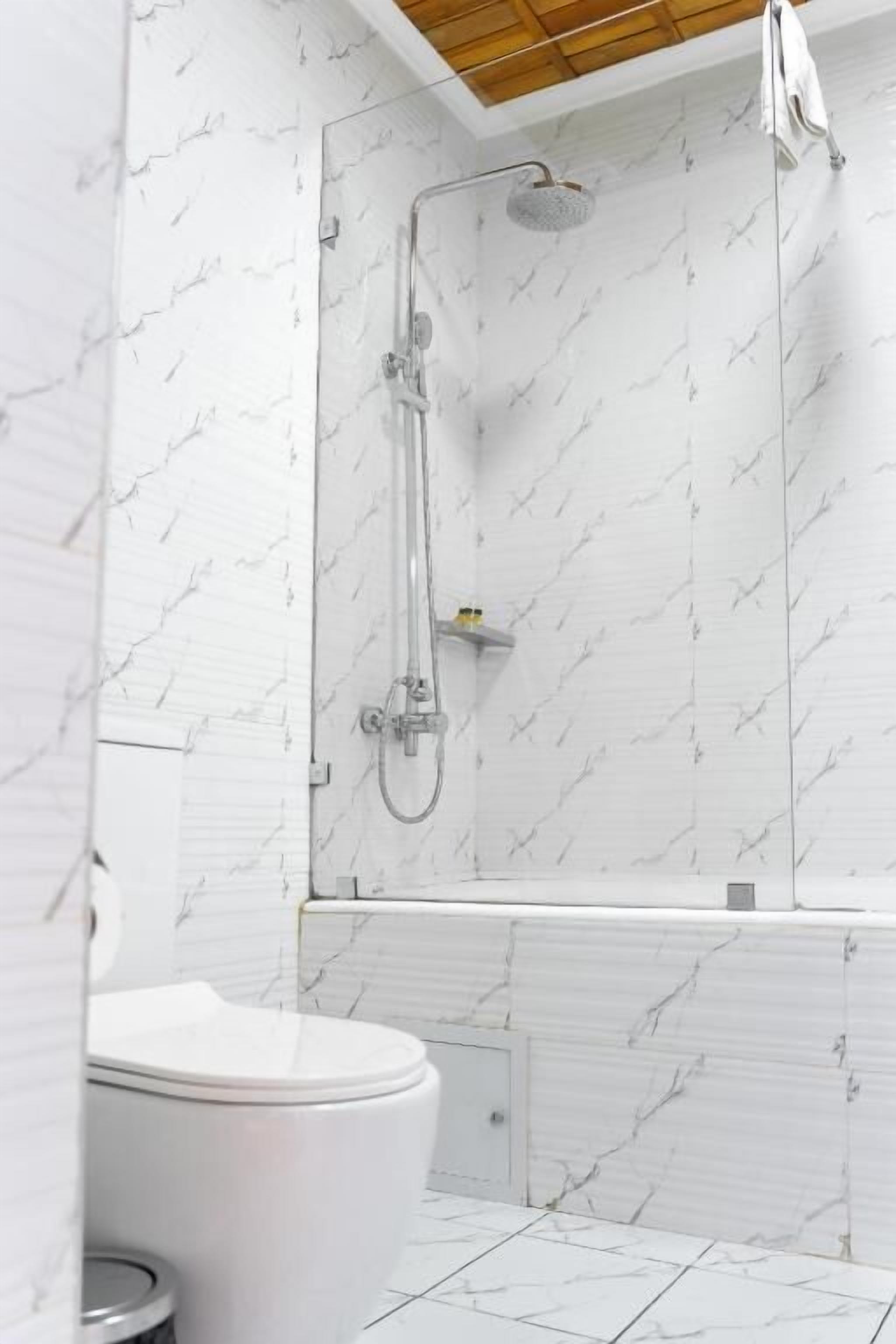 Moderni kylpyhuone, jossa on suihku, wc ja marmorikuvioidut seinät.