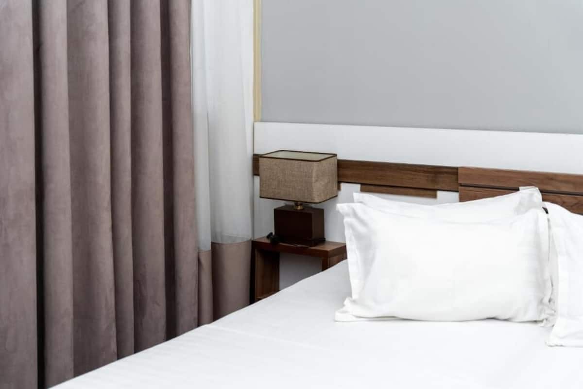 A neatly made bed with white linens, a wooden headboard, and a bedside table with a lamp.