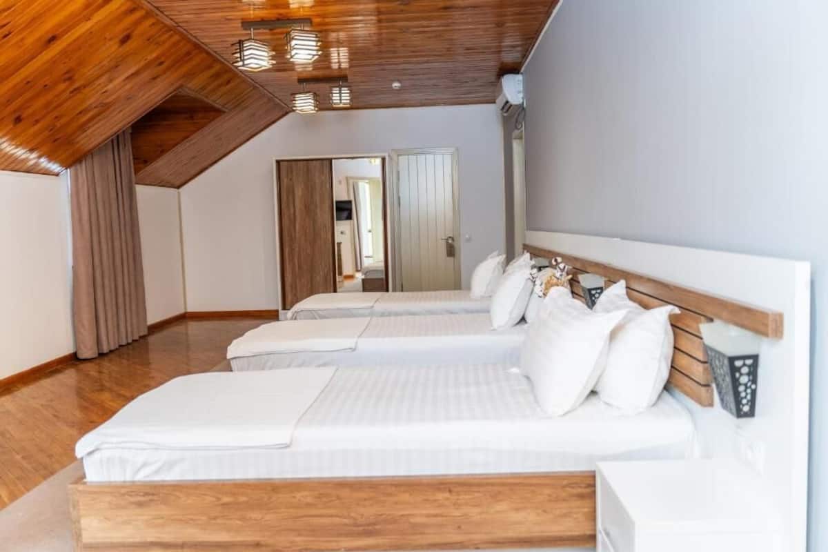 A bedroom with two beds, wooden ceiling beams, and a white wall.