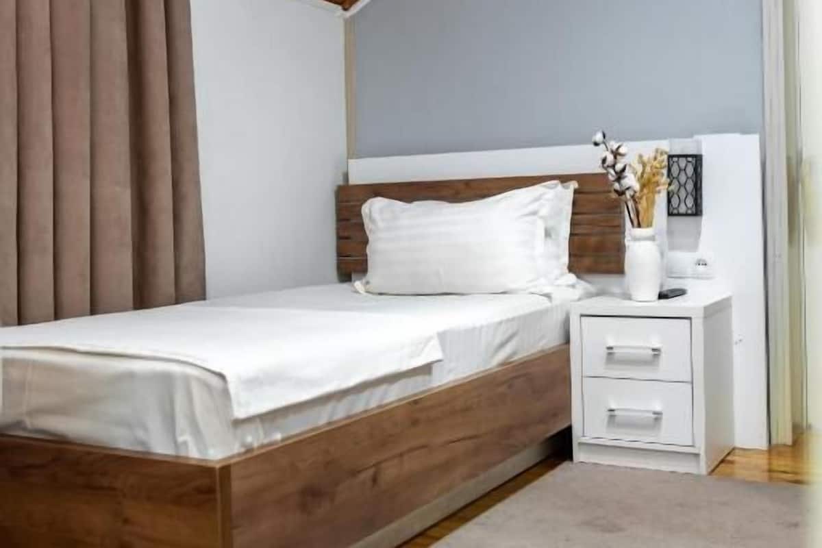 A bedroom with a wooden bed, white bedding, a nightstand, and a vase with flowers.