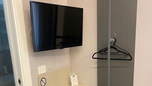 A modern room with a flat-screen TV mounted on the wall, a small shelf with a remote control, a green chair, and a coat hanger. - GREY HOUSE SRLS (Latina)