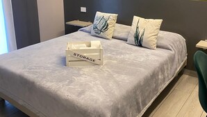 A modern bedroom with a grey bed, two pillows, a bedside table, and a storage box labeled "STORAGE". - GREY HOUSE SRLS (Latina)