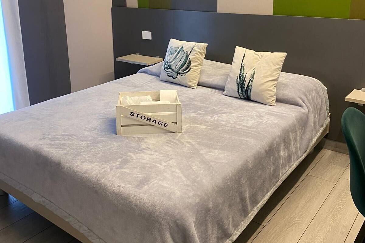 Une chambre à coucher moderne avec un lit gris, deux oreillers, une table de chevet et une boîte de rangement étiquetée « RANGEMENT ».
