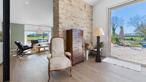 A spacious room with a large window, a stone wall, a wooden cabinet, a chair, and a lamp.