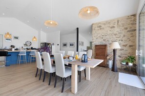 Una cucina moderna con zona pranzo, che include un tavolo di legno, sedie bianche e illuminazione a sospensione.