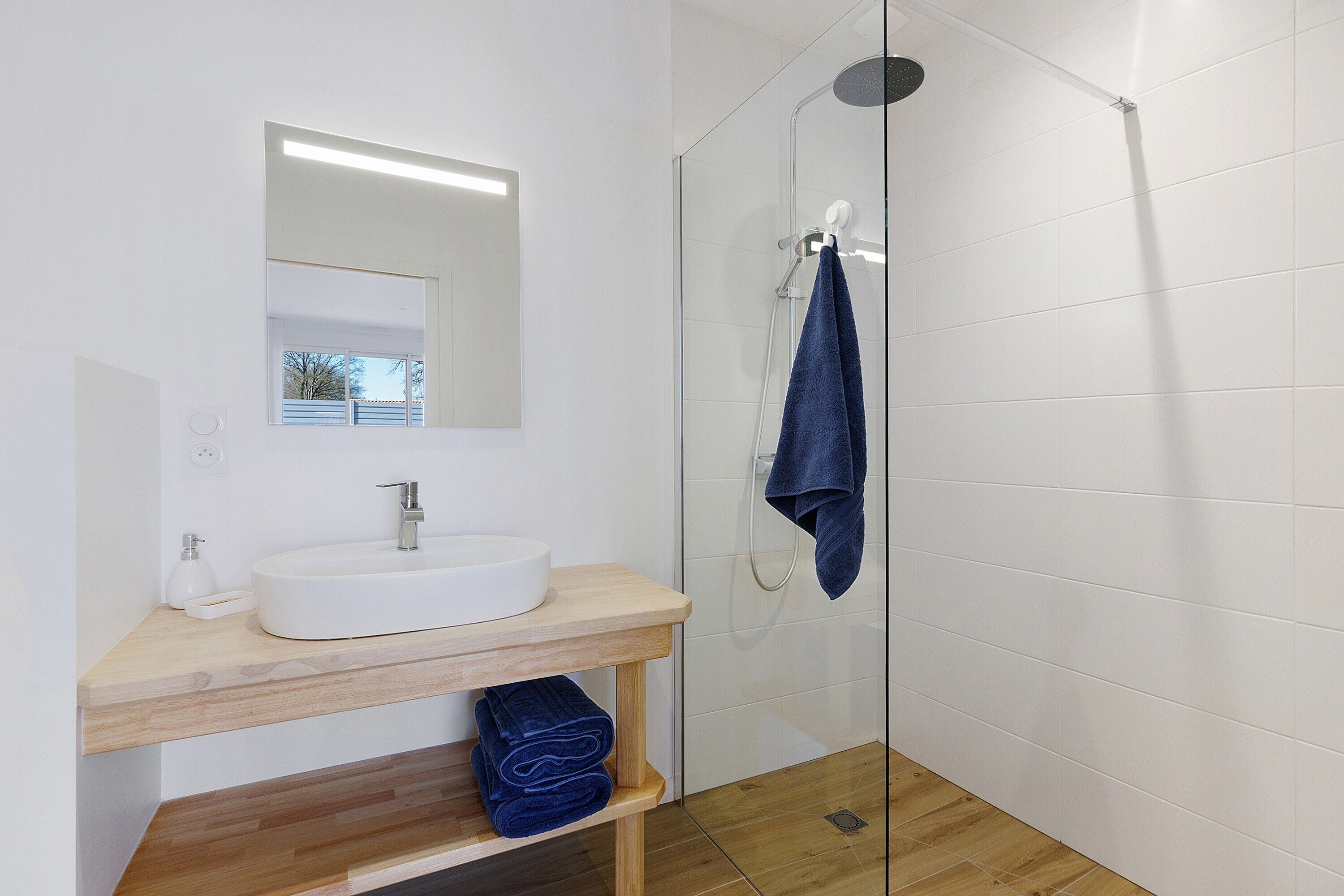 A modern bathroom with a glass shower enclosure, a white sink, and a wooden vanity.
