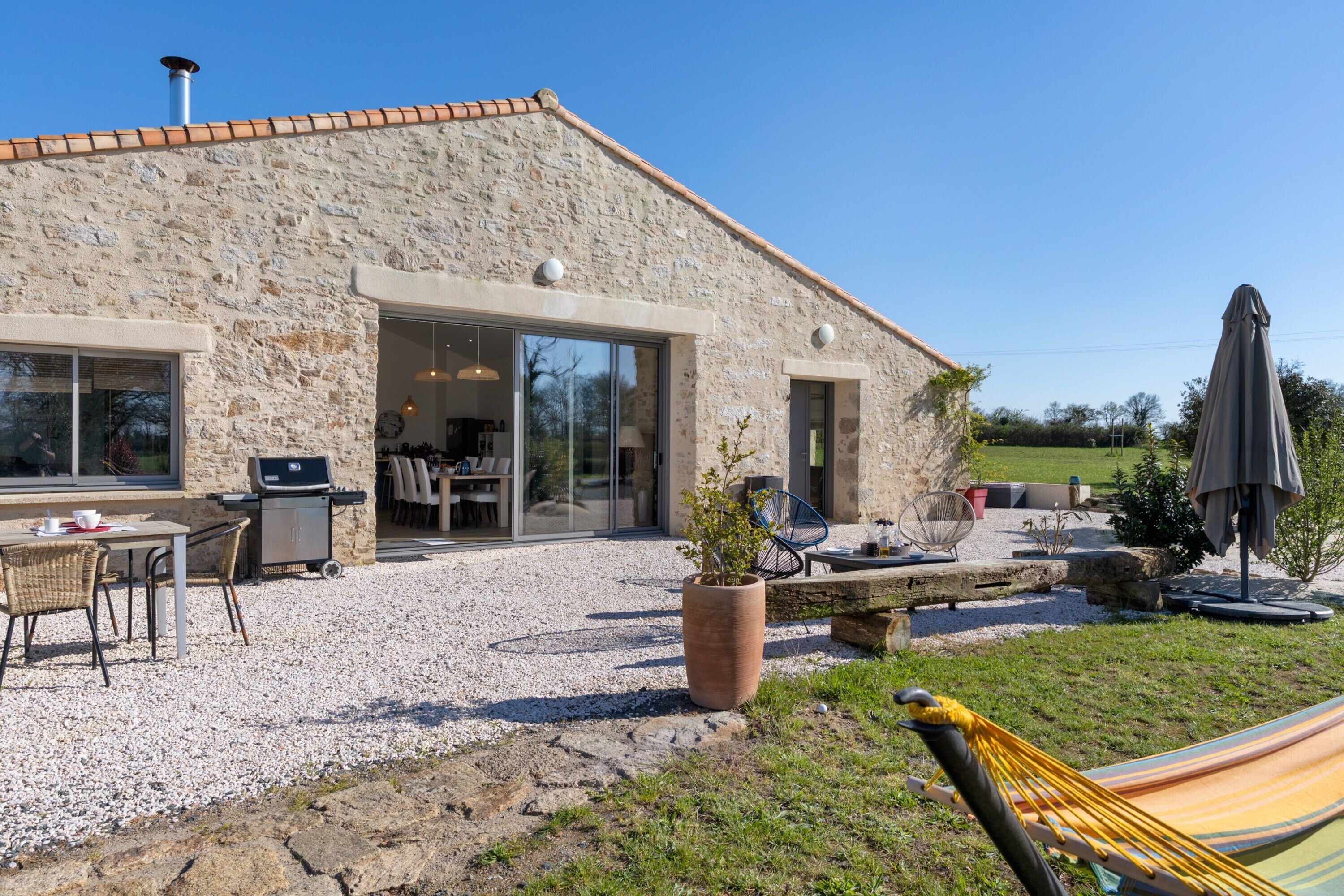 Un bâtiment en pierre doté d’une terrasse, de sièges extérieurs, d’un barbecue et d’un hamac.