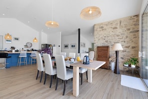 Una cucina moderna con zona pranzo, che include un tavolo di legno, sedie bianche e illuminazione a sospensione.