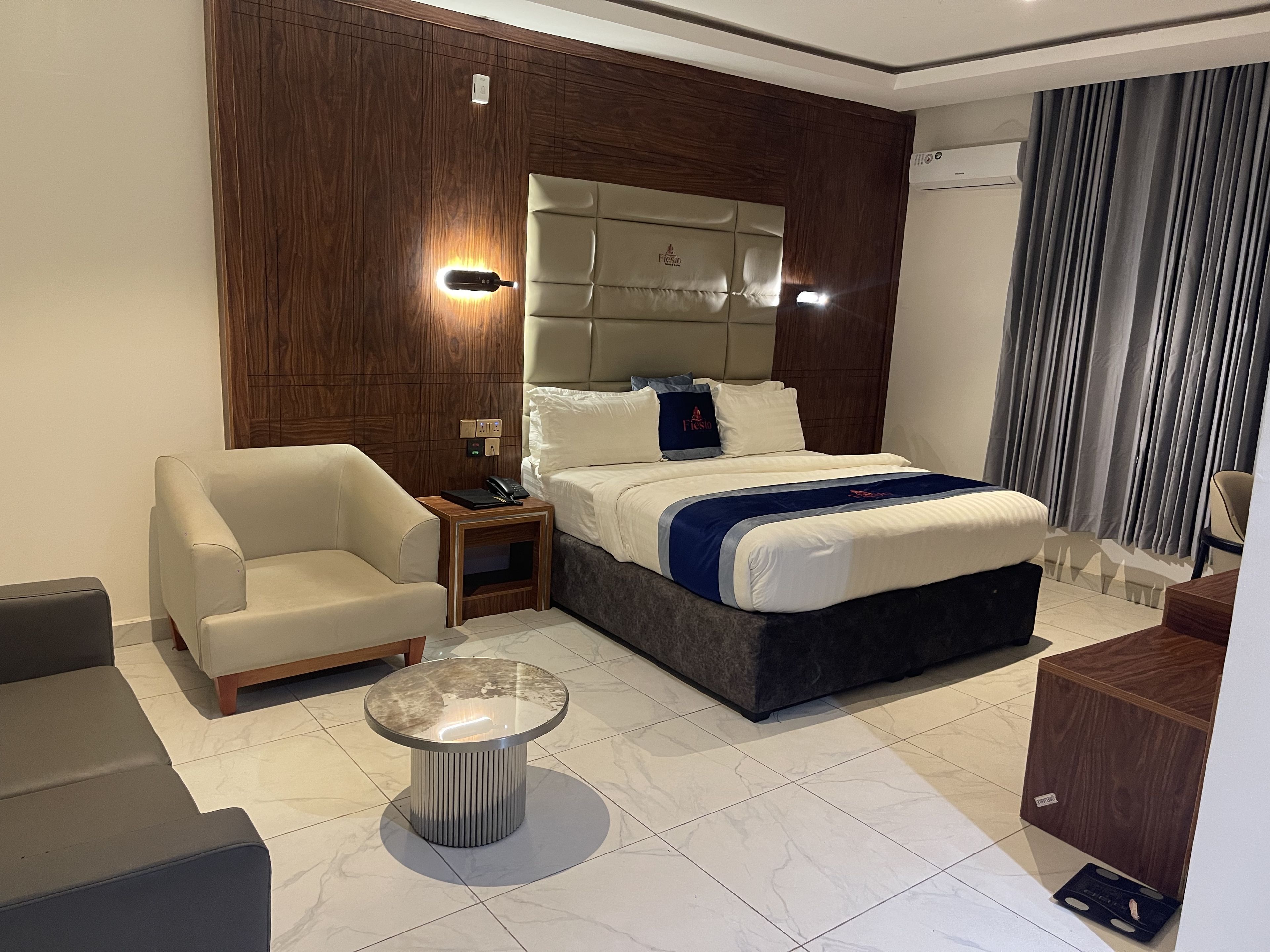 A hotel room with a bed, a sofa, a nightstand, a lamp, and a small table.