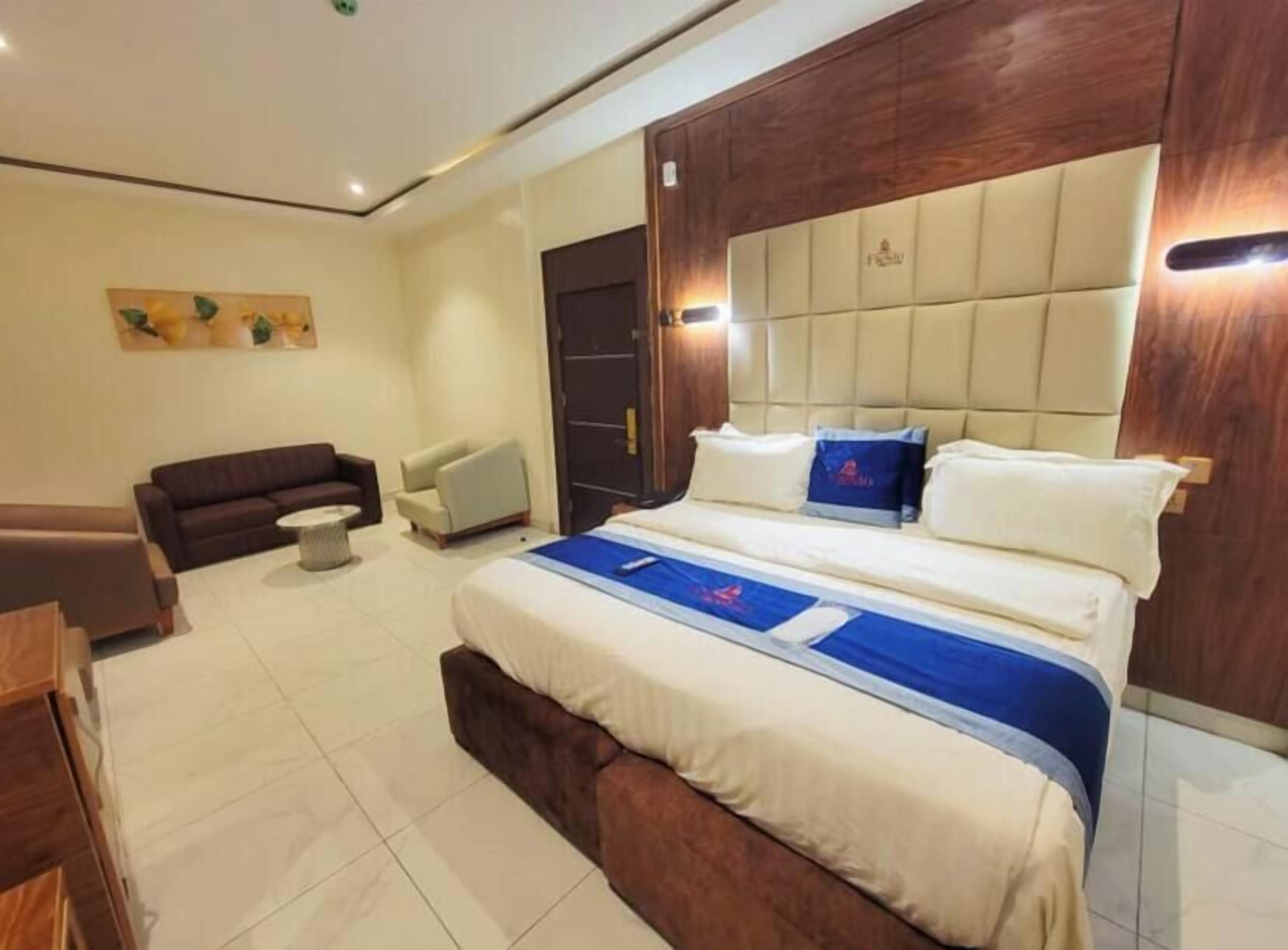 A modern hotel room with a large bed, a sofa, a chair, and a small table.