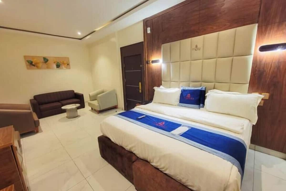 A modern hotel room with a large bed, a sofa, a chair, and a small table.