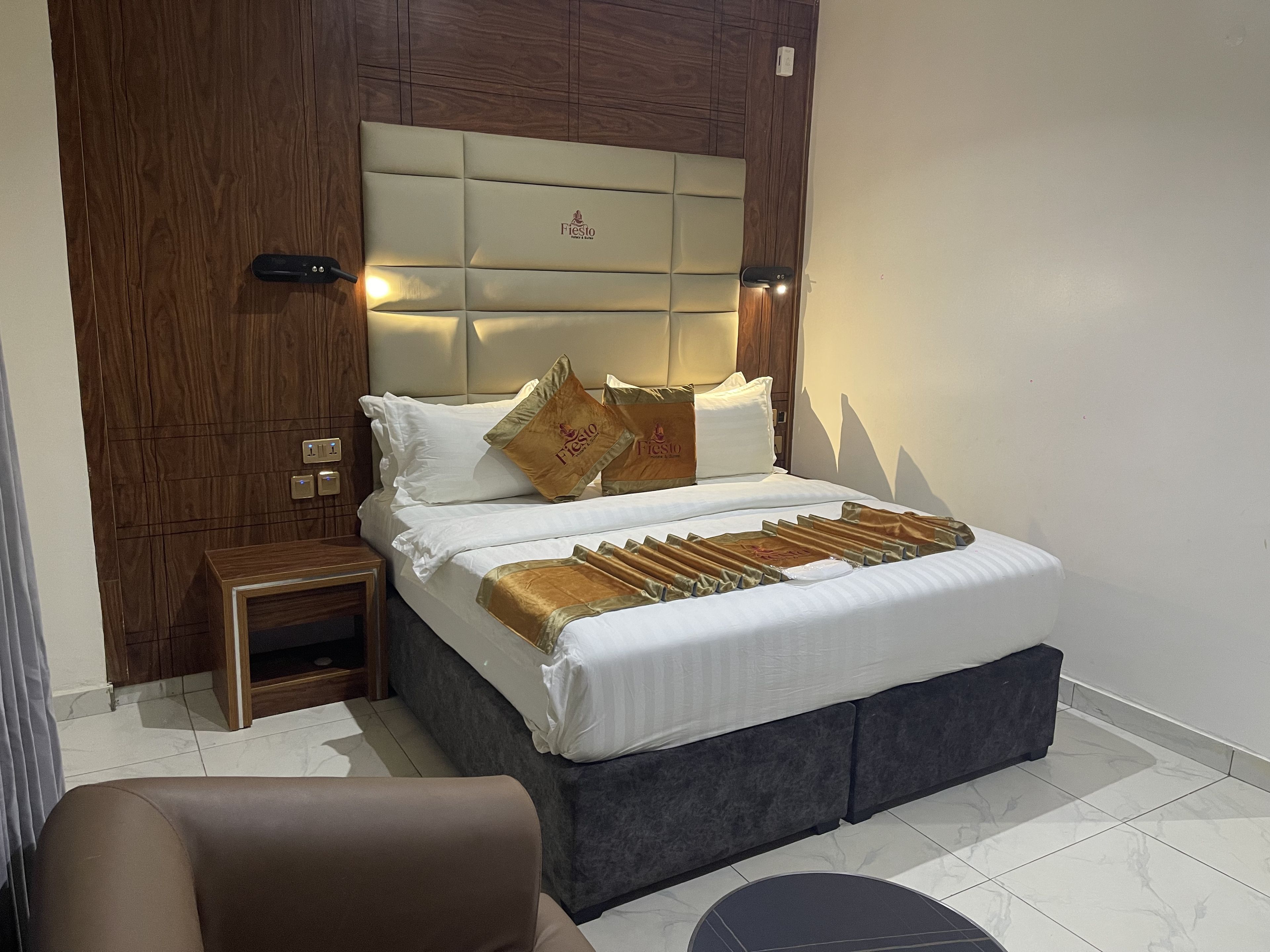 A hotel room with a bed, bedside table, and a chair.