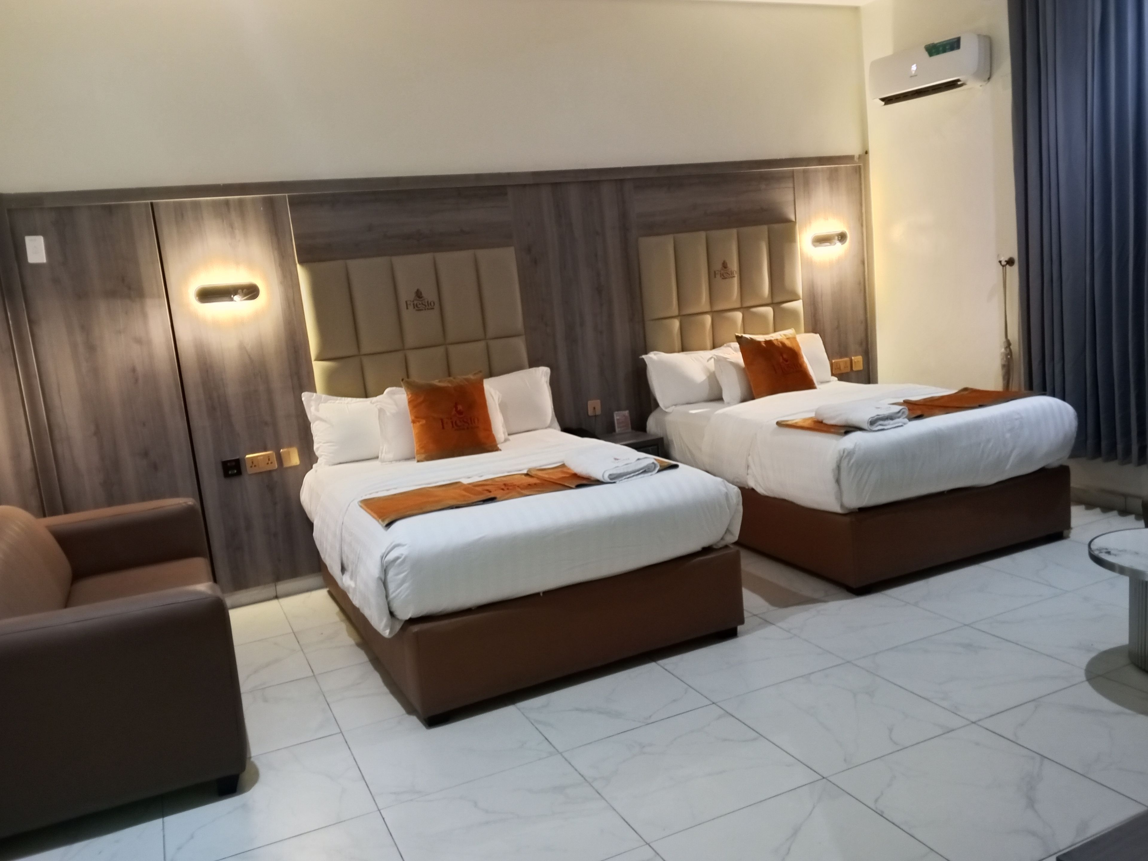 A hotel room with two beds, a sofa, and a tiled floor.