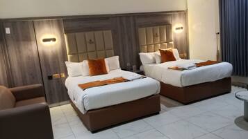 A hotel room with two beds, a sofa, and a tiled floor.