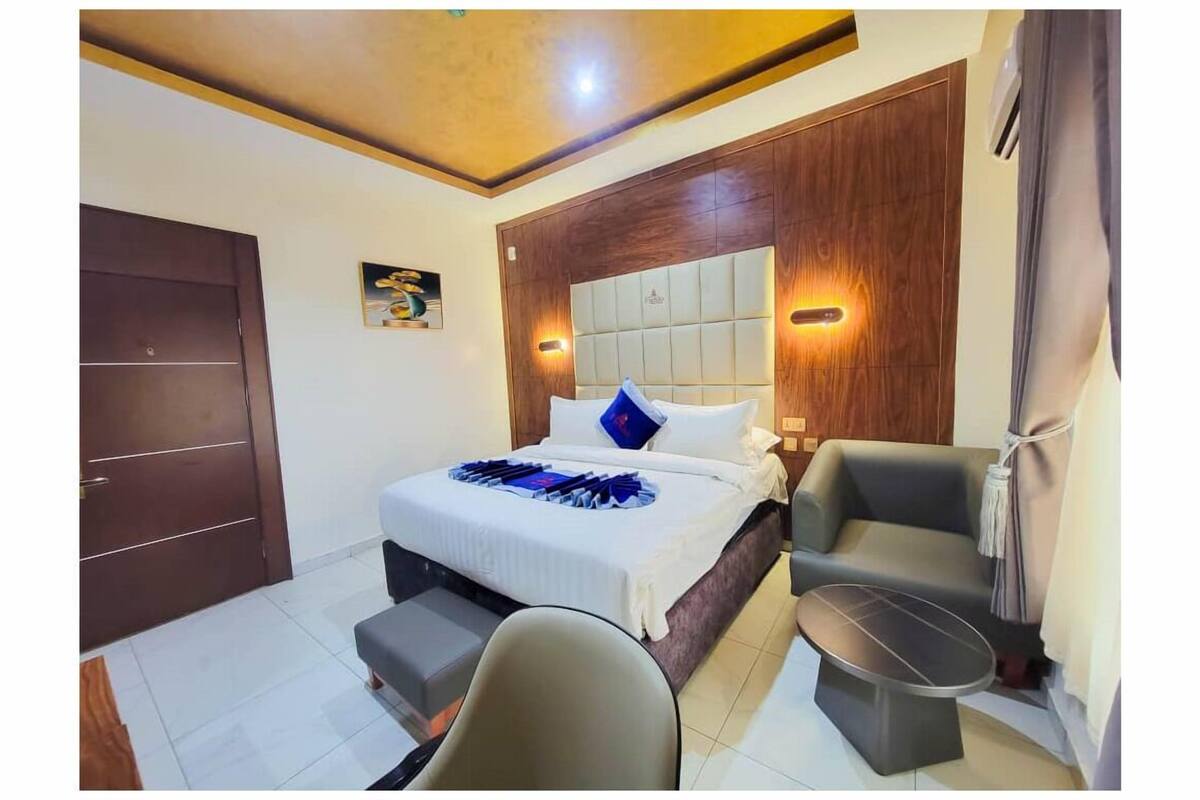 A hotel room with a bed, a desk, a chair, and a small table.