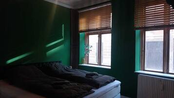 Un dormitorio con cama, ventana con persianas y radiador.