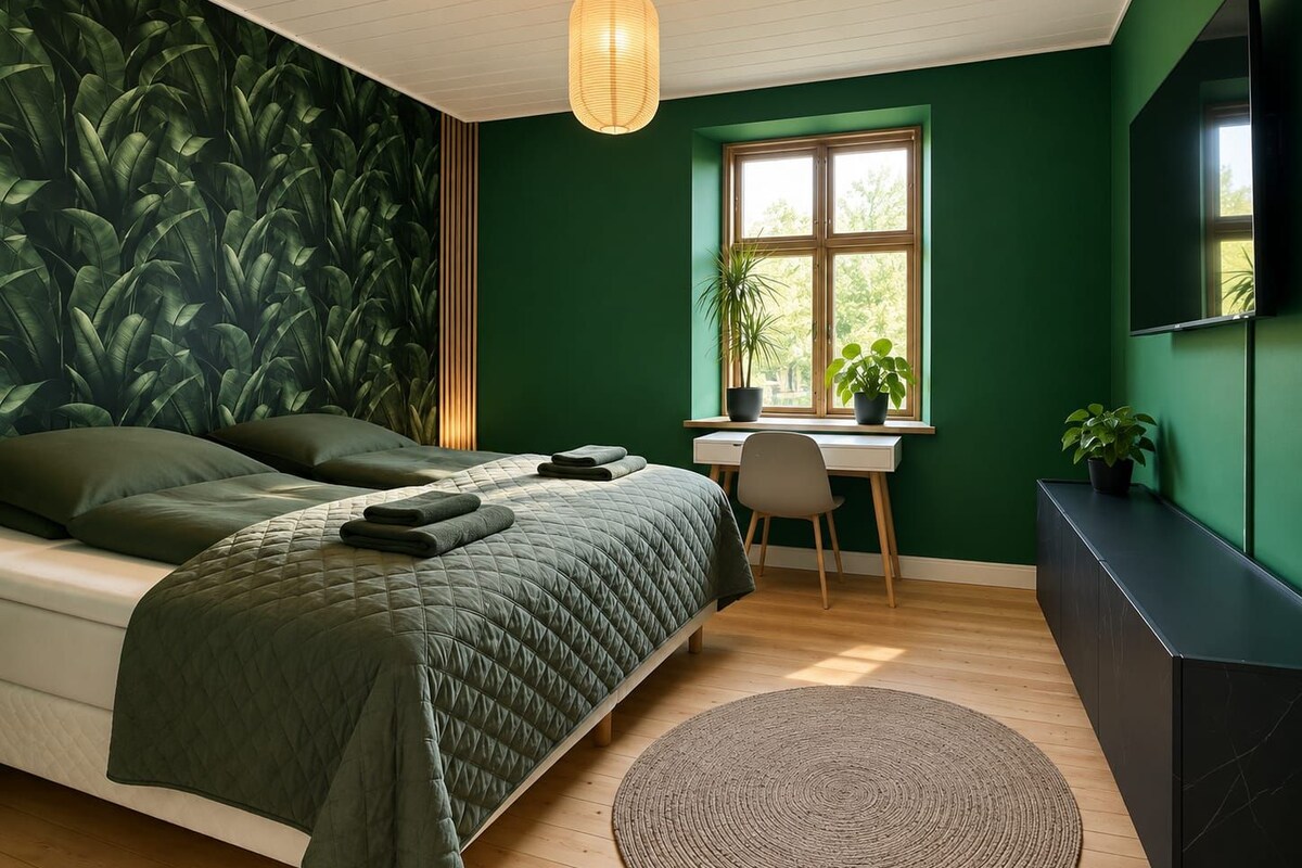 Un dormitorio con una cama, un escritorio, una silla, un tapete redondo y una ventana con plantas.