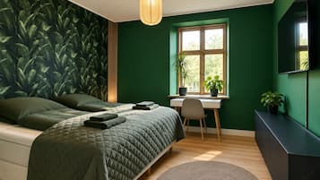 A bedroom with a bed, a desk, a chair, a round rug, and a window with plants.