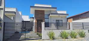 A modern two-story house with a gated entrance, a pool, and a small garden area. - Prehenn Beach House with Pool   (Itapoá)