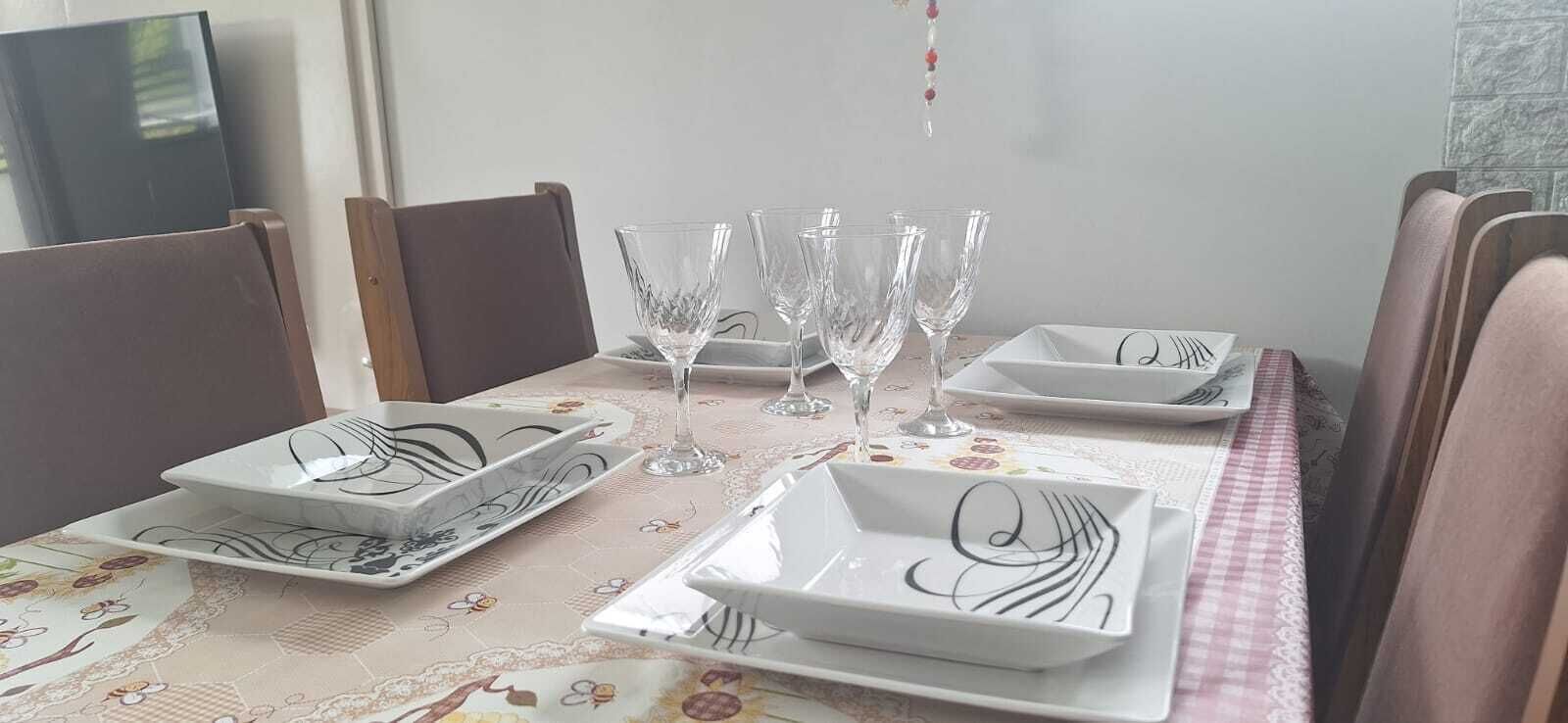 Una mesa de comedor dispuesta con platos blancos y cubertería de vidrio, rodeada de sillas de madera.