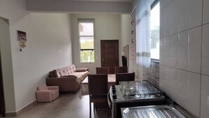 A living room with a sofa, chairs, a dining table, and a kitchen area with a stove. - Prehenn Beach House with Pool (Itapoá)