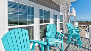 Una terrazza con poltroncine Adirondack color turchese, ampie finestre e vista sull'oceano.