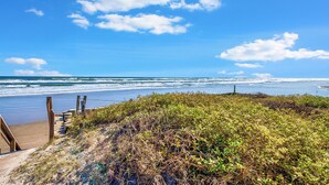 Una spiaggia con una passerella in legno che conduce all'acqua, circondata da vegetazione lussureggiante.